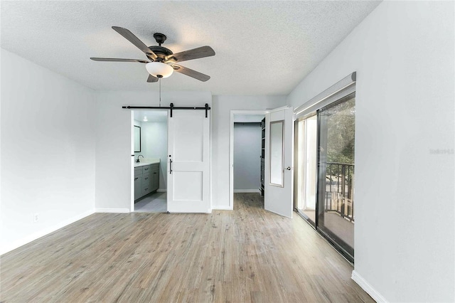 empty room featuring light wood-type flooring, a textured ceiling, a barn door, and ceiling fan