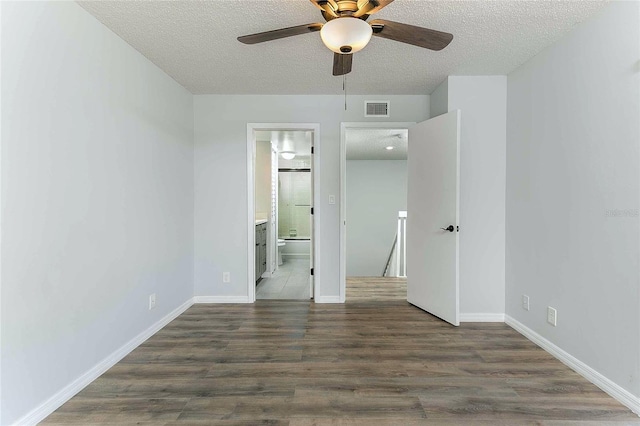 unfurnished bedroom with a textured ceiling, ensuite bathroom, ceiling fan, and dark hardwood / wood-style floors