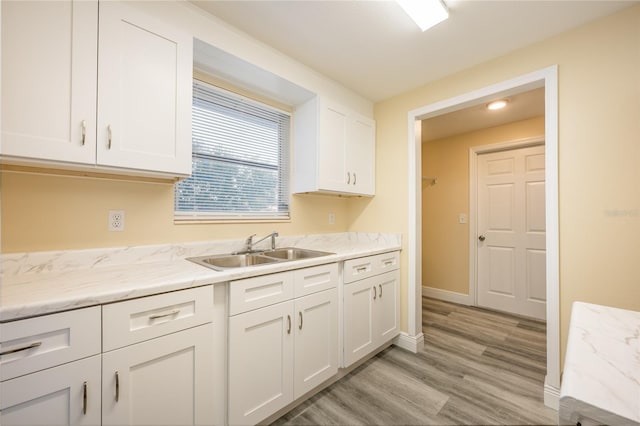 kitchen with white cabinets, light wood-type flooring, light stone countertops, and sink