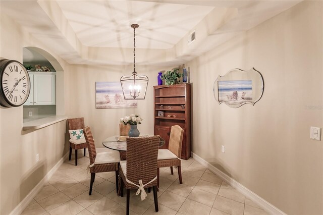 tiled dining room featuring an inviting chandelier and a raised ceiling