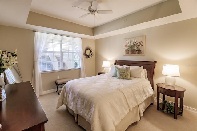 bedroom featuring light carpet, ceiling fan, and a tray ceiling