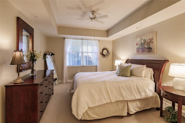 carpeted bedroom with ceiling fan and a tray ceiling