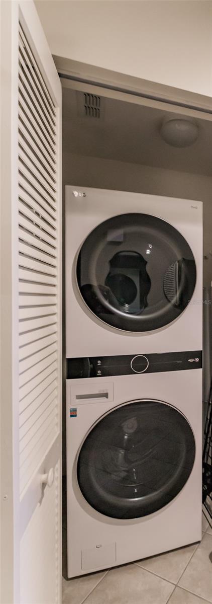 clothes washing area with light tile patterned flooring and stacked washer and clothes dryer