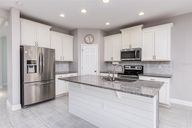 kitchen with white cabinetry, stainless steel appliances, backsplash, light tile patterned floors, and a center island with sink