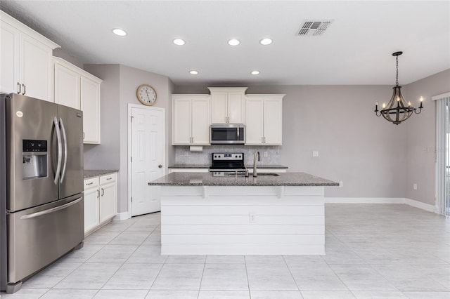 kitchen featuring dark stone countertops, appliances with stainless steel finishes, sink, white cabinetry, and an island with sink