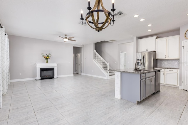 kitchen with a center island with sink, white cabinets, ceiling fan with notable chandelier, and appliances with stainless steel finishes