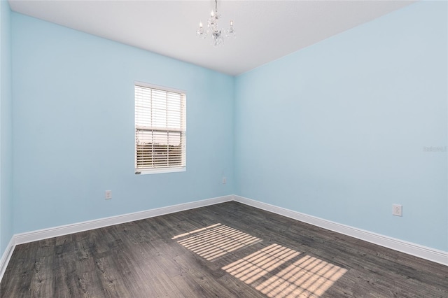 spare room with an inviting chandelier and dark hardwood / wood-style floors