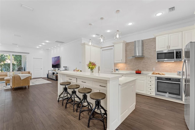 kitchen featuring a breakfast bar, stainless steel appliances, wall chimney range hood, decorative light fixtures, and a center island