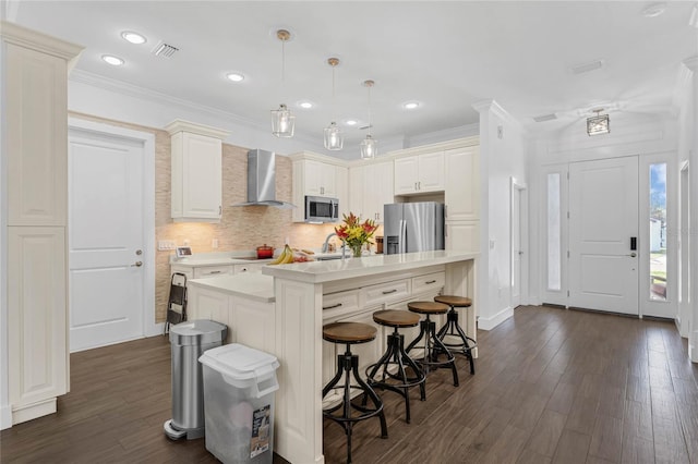 kitchen with a kitchen bar, appliances with stainless steel finishes, wall chimney range hood, pendant lighting, and a center island