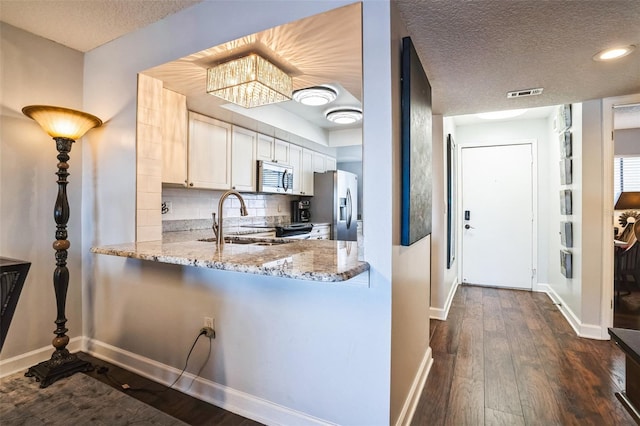 kitchen with visible vents, dark wood-type flooring, a sink, light stone counters, and stainless steel appliances