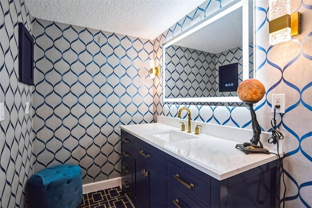 bathroom with baseboards, a textured ceiling, vanity, and wallpapered walls