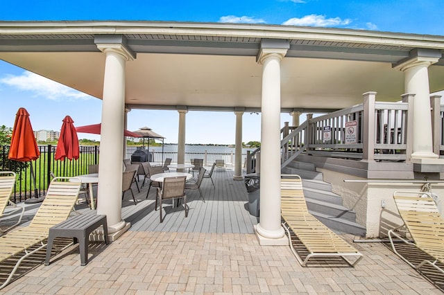 view of patio with a deck with water view, stairs, outdoor dining area, and fence