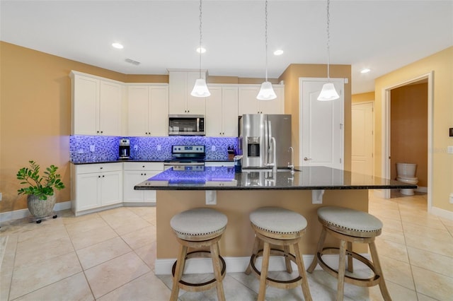 kitchen with a center island with sink, light tile patterned floors, tasteful backsplash, white cabinetry, and appliances with stainless steel finishes