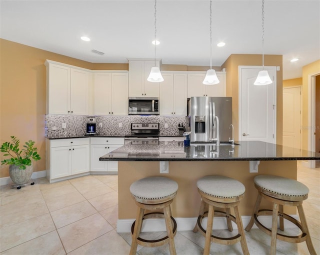 kitchen featuring white cabinetry, a kitchen island with sink, stainless steel appliances, hanging light fixtures, and backsplash