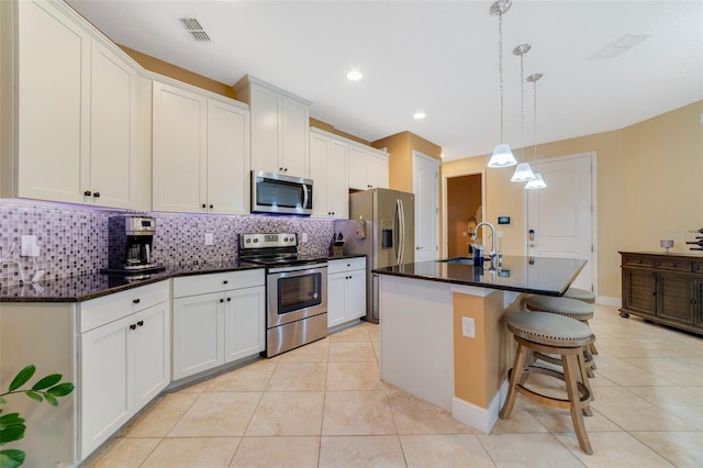 kitchen with appliances with stainless steel finishes, sink, white cabinetry, pendant lighting, and a kitchen island with sink