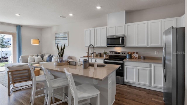 kitchen featuring white cabinetry, stainless steel appliances, dark hardwood / wood-style floors, a textured ceiling, and a center island with sink