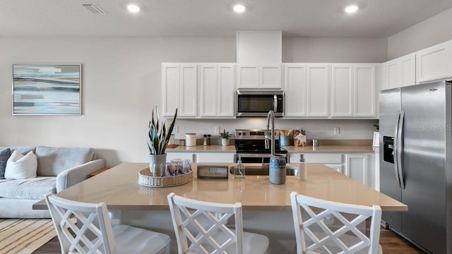 kitchen with white cabinets, a breakfast bar, stainless steel appliances, and an island with sink