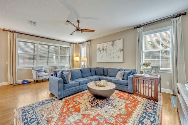 living room with ceiling fan, light wood-type flooring, and a textured ceiling