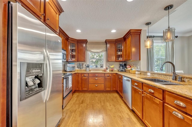 kitchen featuring light stone countertops, appliances with stainless steel finishes, sink, decorative light fixtures, and light hardwood / wood-style floors