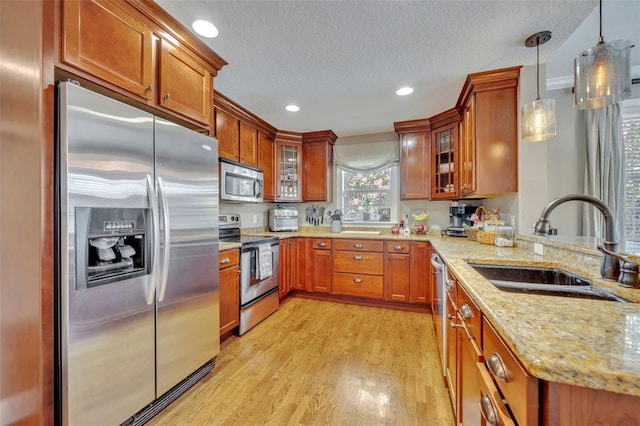 kitchen with appliances with stainless steel finishes, light stone counters, sink, decorative light fixtures, and light hardwood / wood-style floors