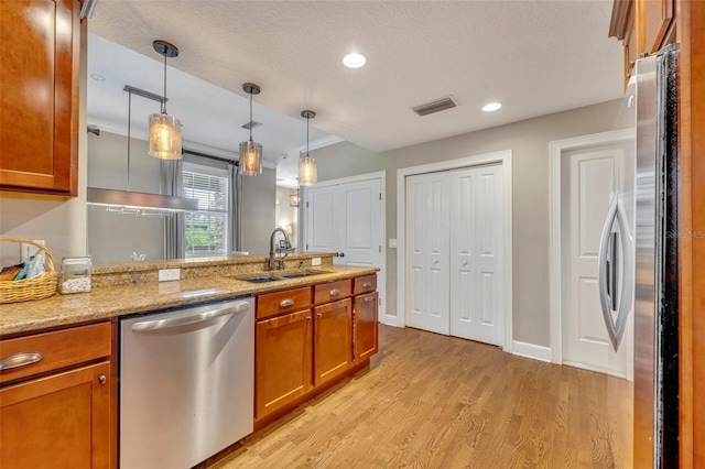 kitchen with light stone countertops, stainless steel appliances, sink, light hardwood / wood-style floors, and hanging light fixtures