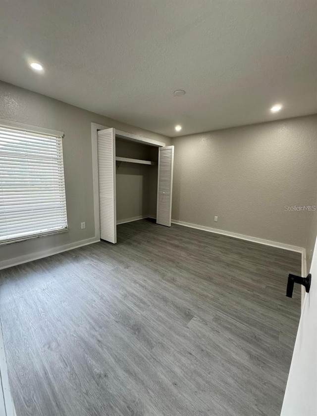 unfurnished bedroom featuring dark wood-type flooring, a textured ceiling, and a closet