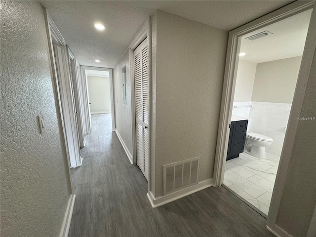 corridor with tile walls, dark wood-type flooring, and a textured ceiling