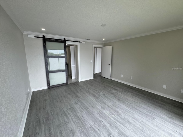 unfurnished room featuring dark wood-type flooring, a textured ceiling, a barn door, and crown molding