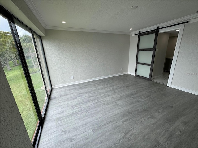 spare room with a textured ceiling, a barn door, crown molding, and hardwood / wood-style floors