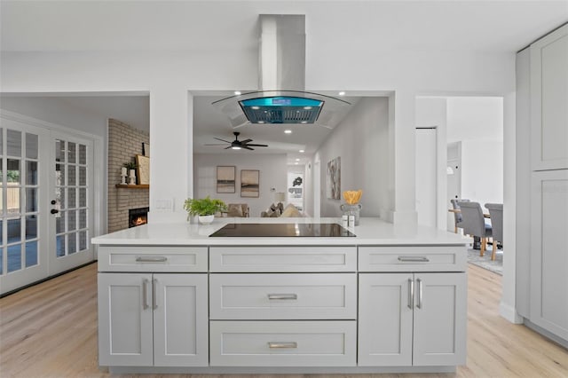 kitchen featuring kitchen peninsula, black electric stovetop, island range hood, ceiling fan, and light hardwood / wood-style floors