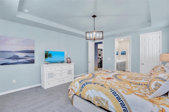 carpeted bedroom featuring a tray ceiling and ensuite bathroom