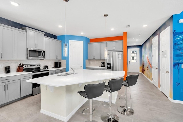 kitchen featuring gray cabinetry, sink, hanging light fixtures, stainless steel appliances, and an island with sink