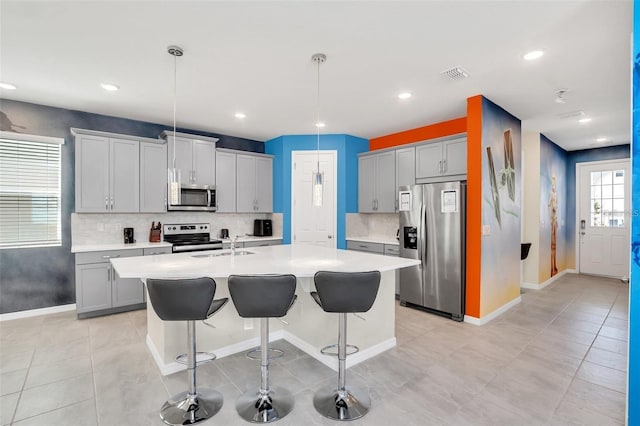 kitchen with appliances with stainless steel finishes, pendant lighting, a center island with sink, gray cabinets, and a breakfast bar area