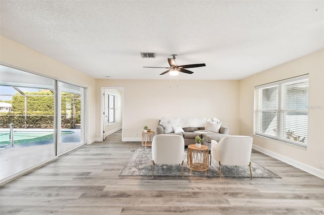 living room with ceiling fan, light wood-type flooring, and a textured ceiling