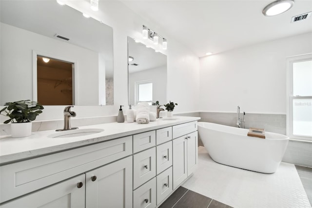 bathroom with tile patterned floors, a bathing tub, vanity, and tile walls