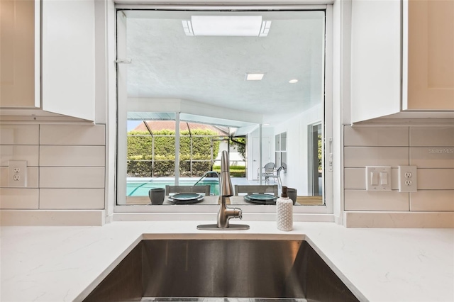 interior details featuring white cabinets, decorative backsplash, light stone countertops, and sink