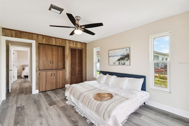 bedroom featuring ceiling fan, wood walls, light hardwood / wood-style flooring, and multiple windows