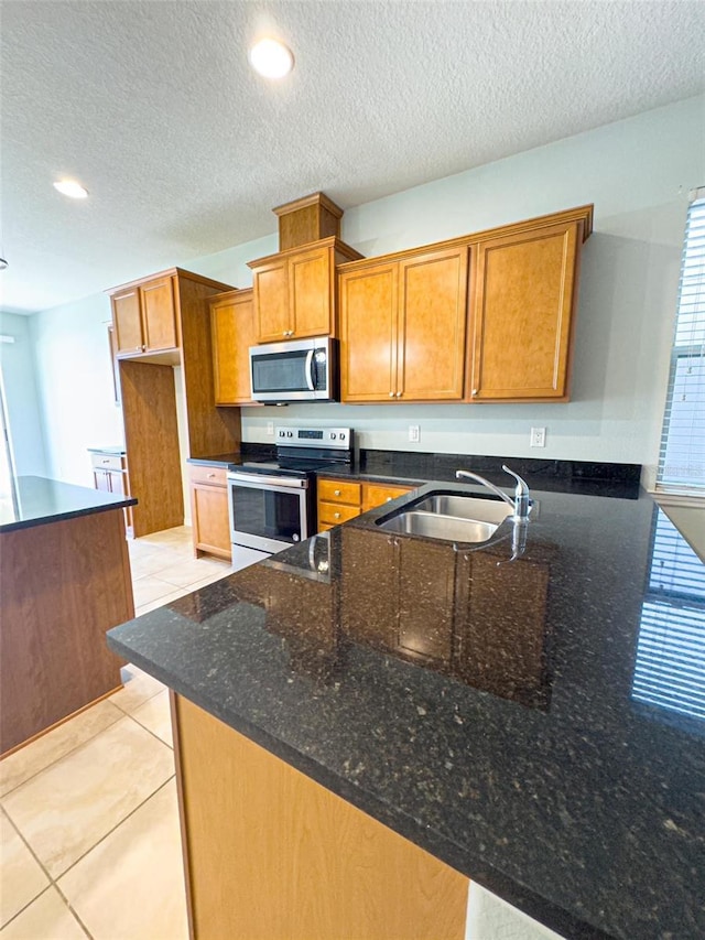 kitchen featuring dark stone counters, sink, light tile patterned floors, kitchen peninsula, and stainless steel appliances