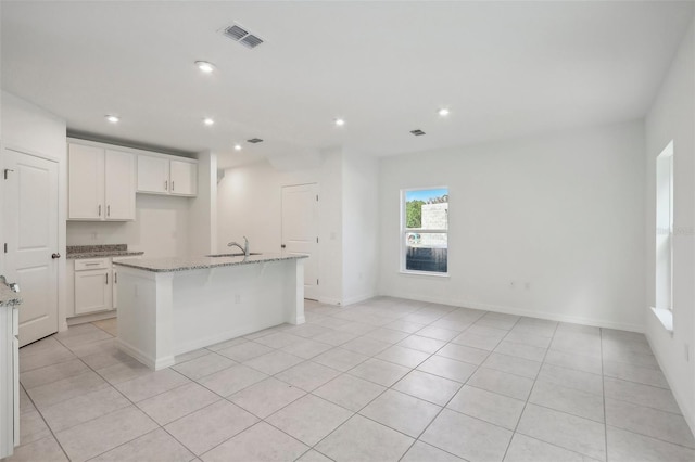 kitchen with a kitchen island with sink, sink, light stone countertops, light tile patterned floors, and white cabinetry