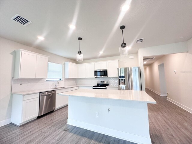 kitchen featuring appliances with stainless steel finishes, a center island, white cabinetry, and hanging light fixtures