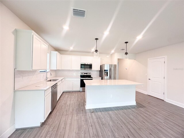 kitchen with appliances with stainless steel finishes, tasteful backsplash, a center island, white cabinetry, and hanging light fixtures