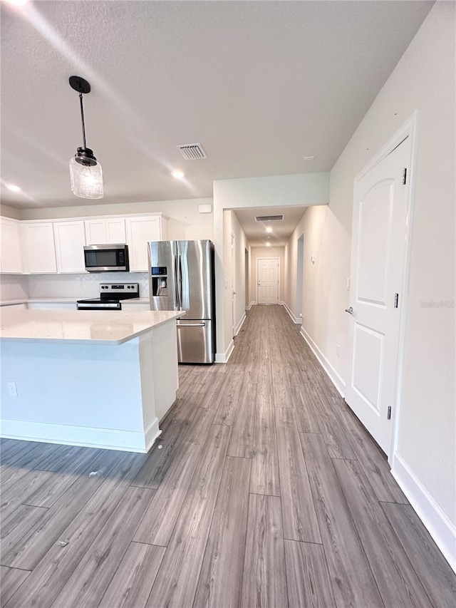 kitchen with white cabinets, appliances with stainless steel finishes, decorative light fixtures, and light hardwood / wood-style floors