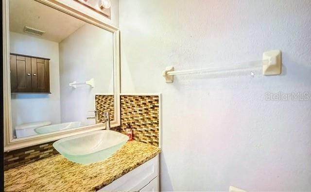 bathroom with toilet, vanity, and decorative backsplash