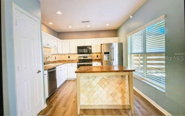 kitchen with white cabinetry, light hardwood / wood-style floors, butcher block countertops, appliances with stainless steel finishes, and sink