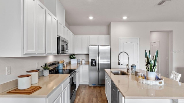 kitchen with white cabinets, appliances with stainless steel finishes, a center island with sink, and sink