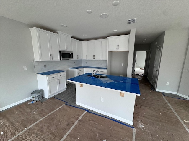 kitchen featuring a center island with sink, sink, a textured ceiling, tasteful backsplash, and white cabinetry