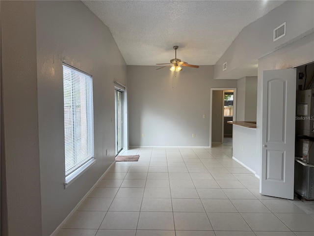 unfurnished room featuring visible vents, vaulted ceiling, light tile patterned flooring, a textured ceiling, and a ceiling fan