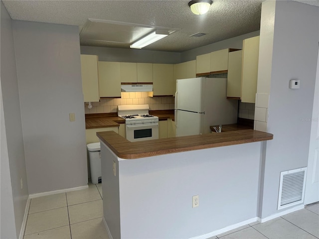 kitchen with visible vents, under cabinet range hood, light tile patterned floors, cream cabinets, and white appliances