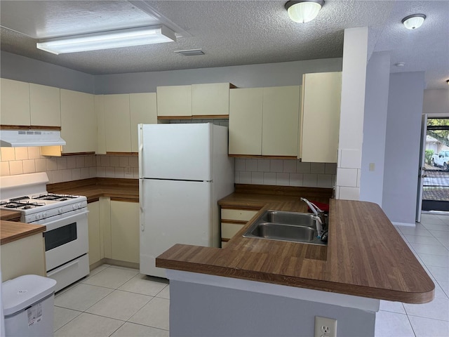 kitchen with under cabinet range hood, a sink, white appliances, a peninsula, and light tile patterned floors