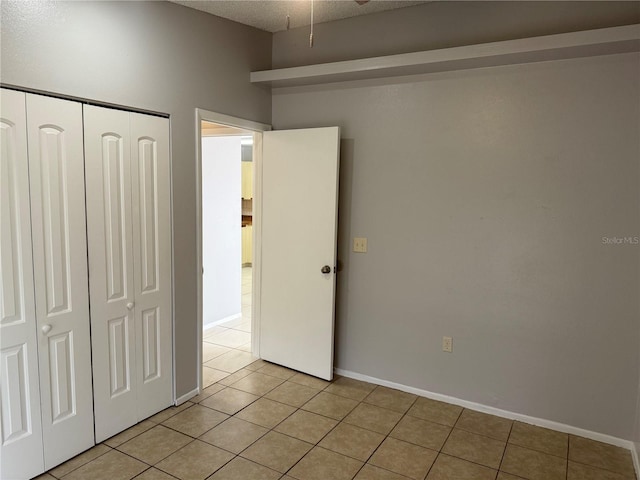 unfurnished bedroom featuring light tile patterned floors, baseboards, a closet, and a textured ceiling